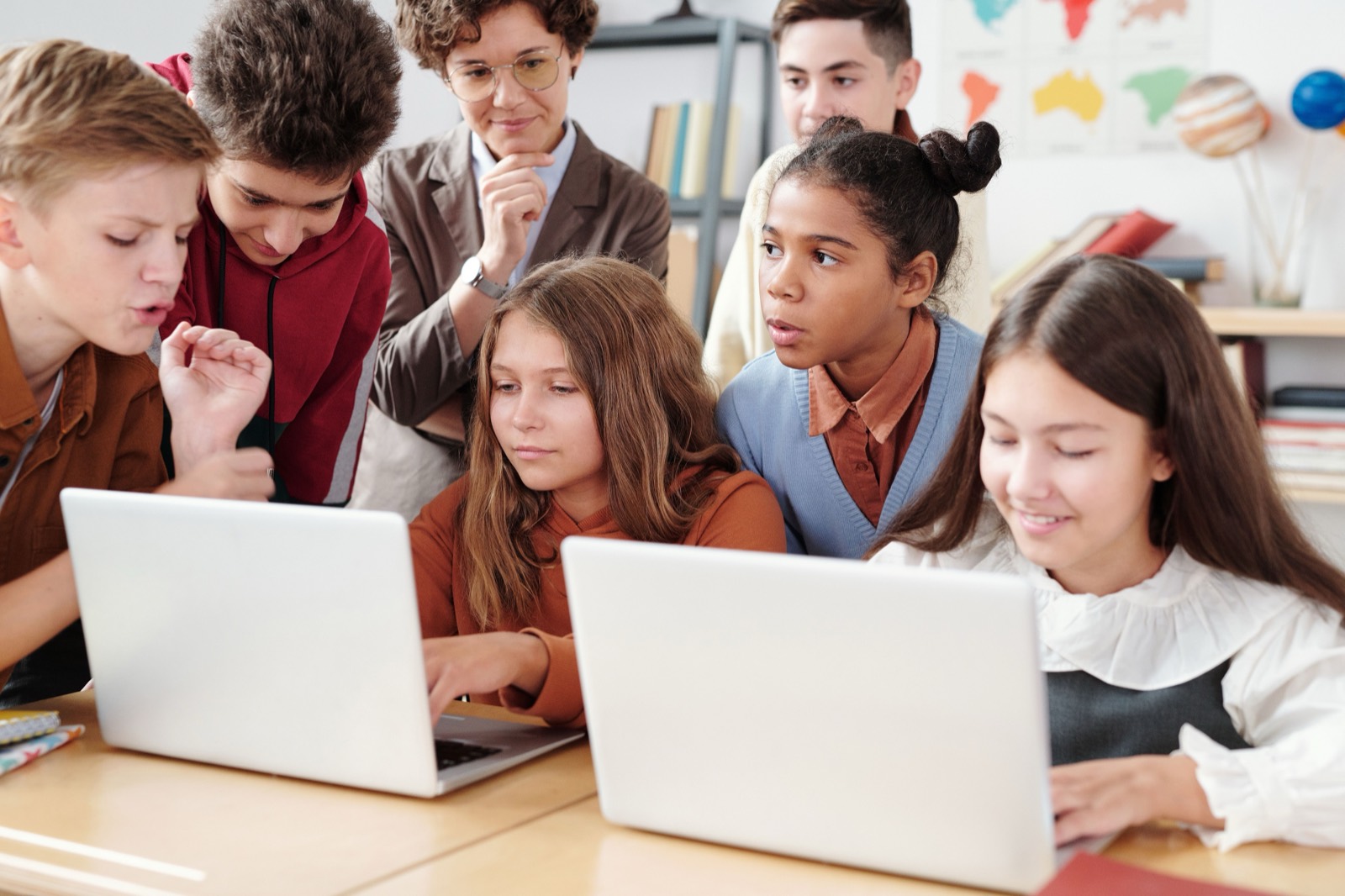 Teacher and students working together on laptops in a classroom